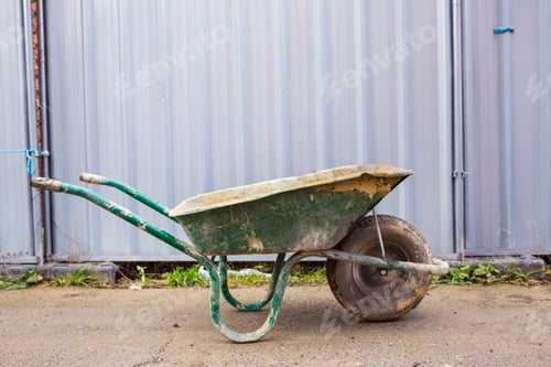 Preview: Green wheelbarrow on a building site in front of a metal container.