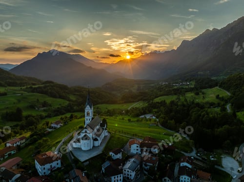 Preview: Aerial view of a church and village in a green valley at sunset.