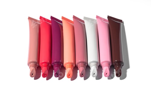 Preview: A collection of beauty products featuring multiple plastic squeeze tubes of lip gloss or lip balm