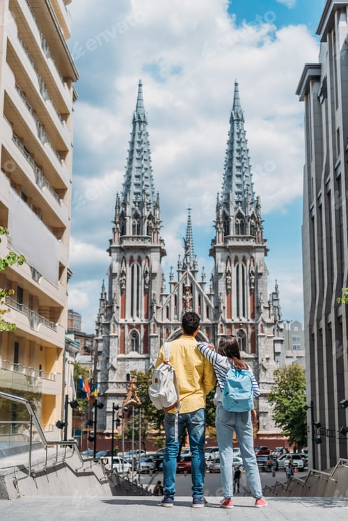 Preview: KYIV, UKRAINE - JULY 8, 2019: back view of girl and mixed race man standing near St. Nicholas Roman