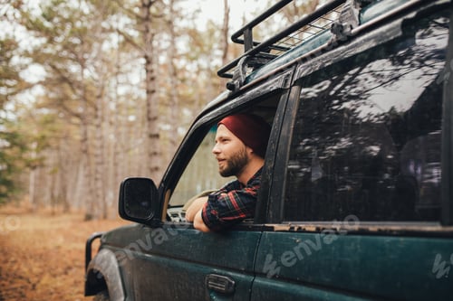 Preview: Millennial man travelling off-road by car in a forest. Wanderlust concept.