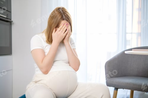 Preview: Tired pregnant woman closes her face with hands.