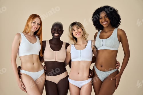 Preview: Four happy diverse young women in underwear hugging on beige background.