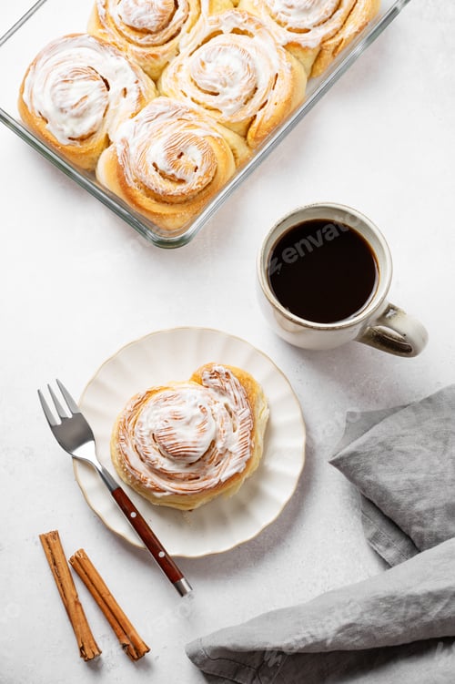 Preview: Freshly baked cinnamon rolls with white icing and a cup of black coffee on a light background.