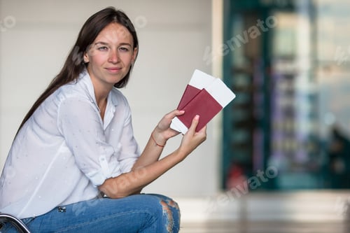 Preview: Happy young woman with air ticket and passports at airport waiting for flight