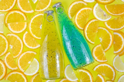 Preview: Two glass bottles on a bright tropical citrus background. Blue and yellow drinks