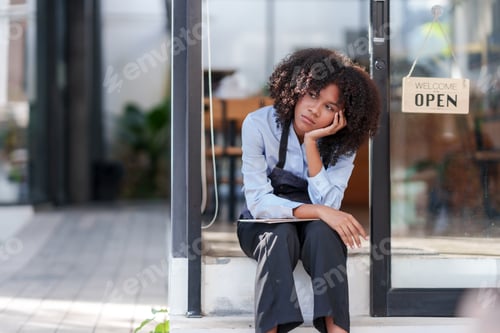 Preview: Female shopkeeper sitting stressed out at the store entrance frustrated by the economic impact.