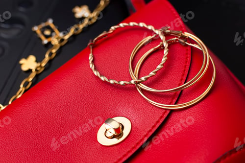 Preview: Gold ring earrings and costume jewelry lie on a red leather bag