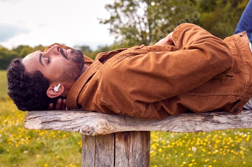 Preview: Man Lying On Bench In Countryside Relaxing And Listening To Music Or Podcast On Wireless Earphones