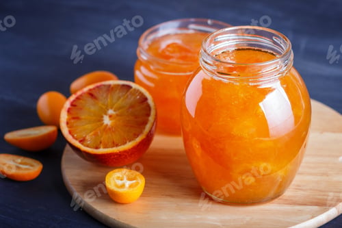 Preview: Orange and kumquat jam in a glass jar with fresh fruits on a wooden kitchen board.