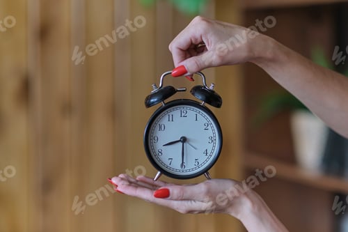 Preview: female hands with red manicure holds a black alarm clock. time management concept