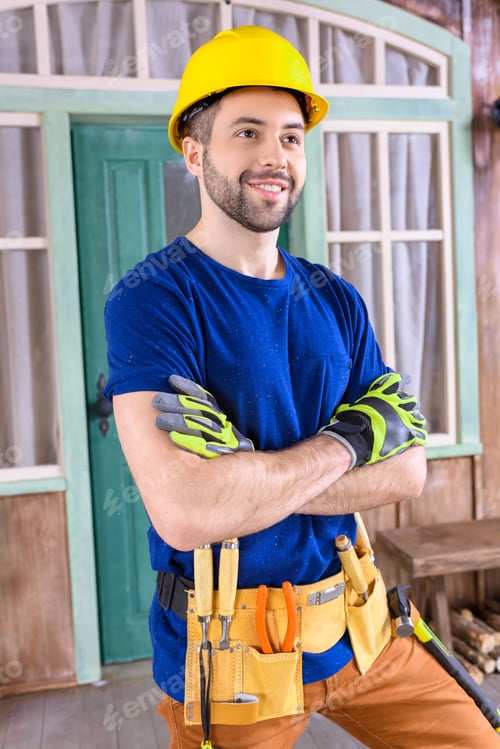 Preview: side view portrait of smiling carpenter in helmet with building tools on porch looking away