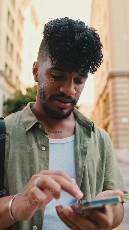 Preview: Young smiling man with beard dressed in an olive color shirt uses phone