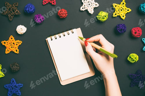Preview: Top view of female hand making some notes in noteebok on colorful background