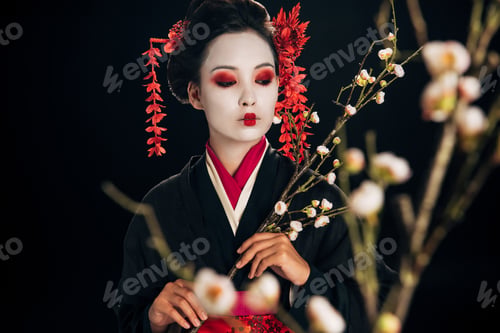 Preview: selective focus of beautiful geisha in black kimono with red flowers in hair looking away and sakura