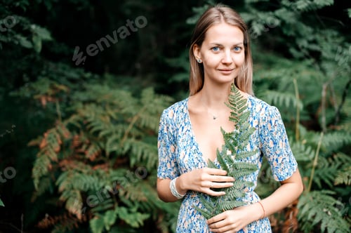 Preview: A girl in a dress holds a fern branch in her hands, hugs it to her and looks at the camera