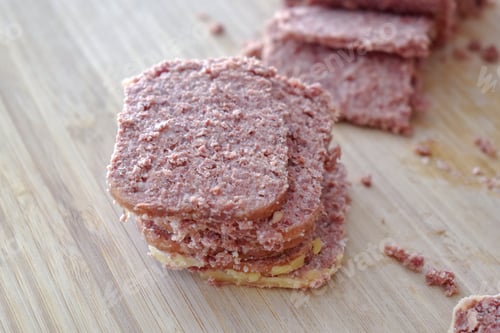 Preview: Canned corned beef slices on a bamboo chopping board.