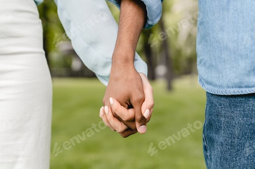 Preview: Cropped close-up shot photo of young couple`s hands walking on a romantic date in city park