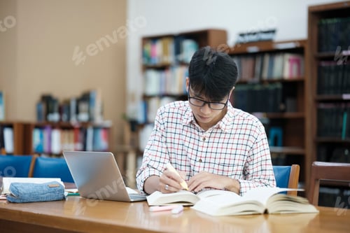Preview: Young Asian male sitting inside a library alone doing research.