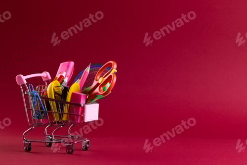 Visualização: Vista de perto do carrinho de compras em miniatura com materiais escolares e espaço de cópia em fundo vermelho