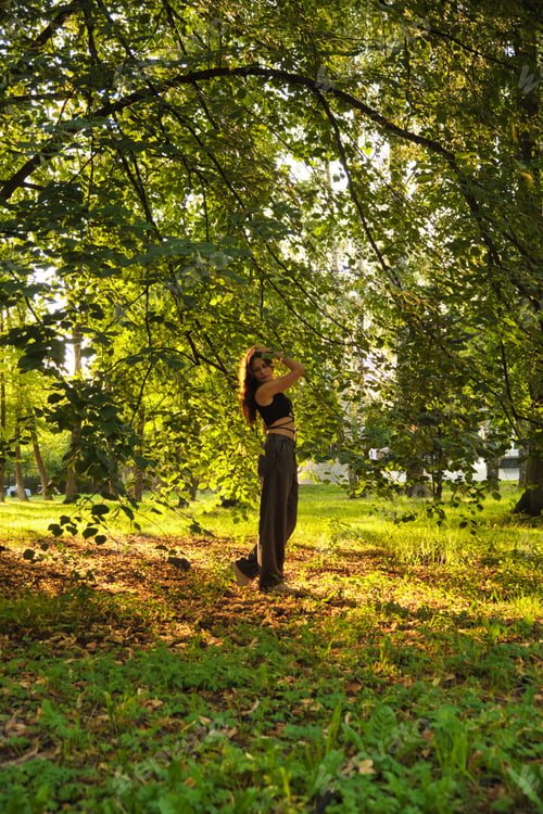 Preview: Woman poses in a sun-dappled forest, her expression serene and confident. The photo emphasizes her
