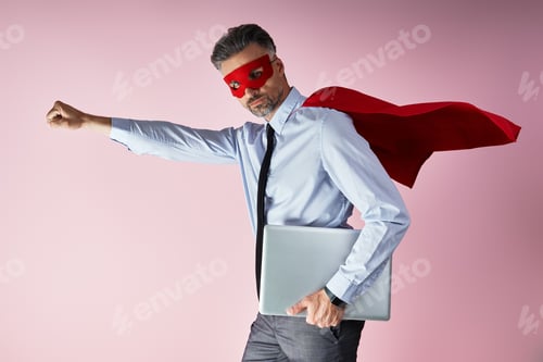 Preview: Confident man in shirt and tie wearing superhero cape and carrying laptop against pink background