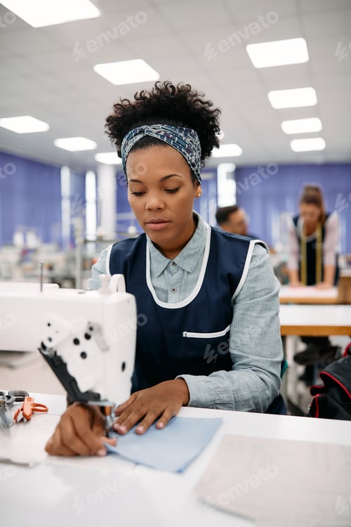 Preview: Young African American seamstress working at sewing machine in a clothing factory.