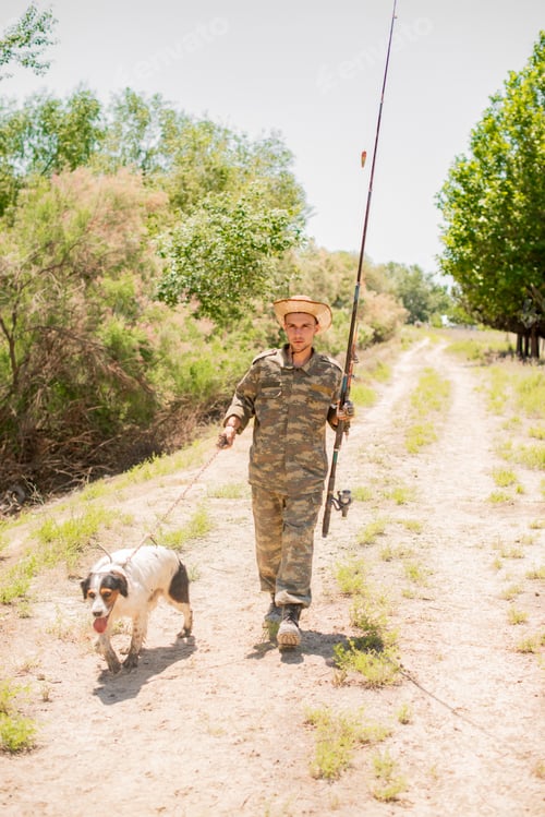 Preview: Focused fisherman in straw hat and camo clothes going fishing with dog on weekend.