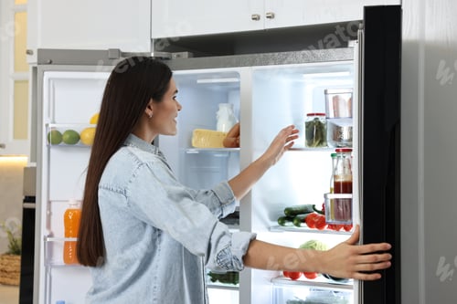 Preview: Young woman near modern refrigerator in kitchen