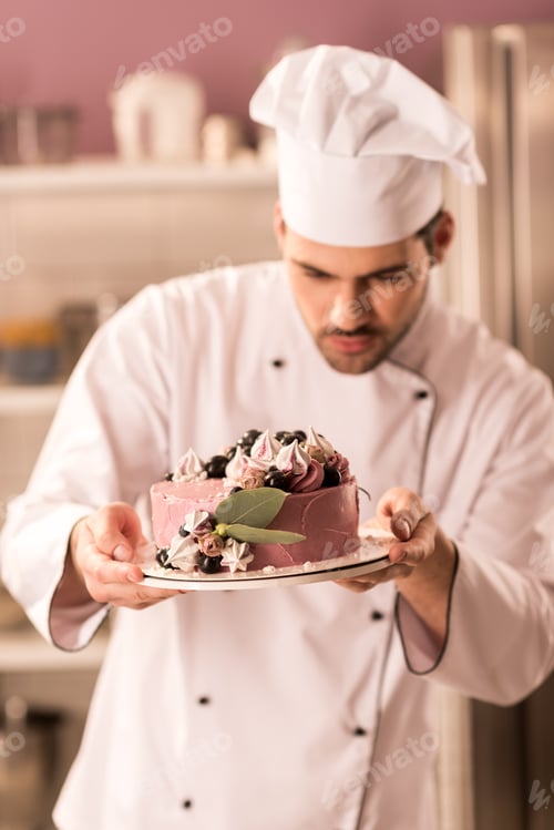 Preview: portrait of confectioner looking at cake in hands in restaurant kitchen