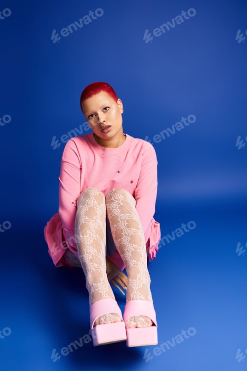 Preview: A young woman with pink hair showcases her bold style in a studio with a blue backdrop