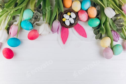 Preview: Easter composition with colored eggs, rabbit ears, nest and tulips on a white wooden background.