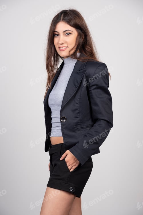 Preview: Young business woman in jacket standing and posing over a gray wall