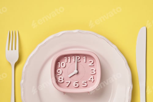 Preview: White plate with lying pink clock 8 ocloc'k, fork and spoon on trendy yellow background. Time to eat