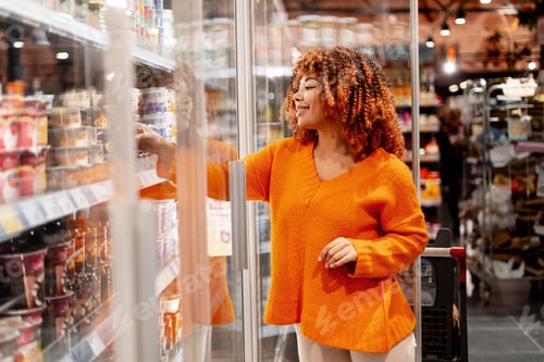 Preview: Young woman shopping for food in a supermarket, choosing items from a cold display