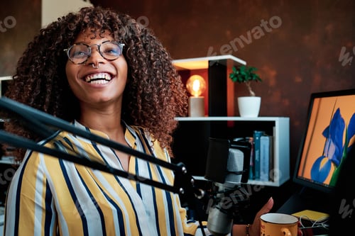 Preview: Smiling afro female blogger enjoying while recording or broadcasting her podcast from home.