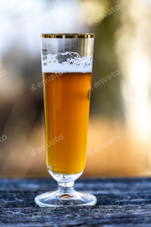 Preview: Vertical closeup of a glass of beer on a wooden surface on a blurred background