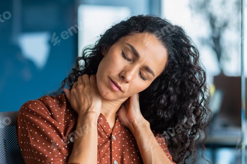 Preview: Tired young hispanic woman sits in the office, holds her neck with her hands, closed her eyes