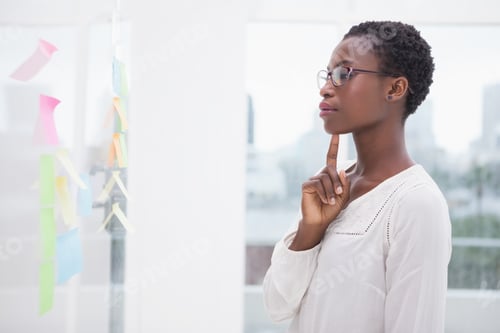 Preview: Thoughtful businesswoman looking at sticky notes on window in the office