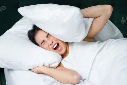 Preview: Sad girl with insomnia. Young asian woman lying in bed, cover her ears with pillow, cant sleep
