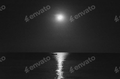 Preview: Grayscale shot of a boat in the calm sea with the reflection of the moon at night