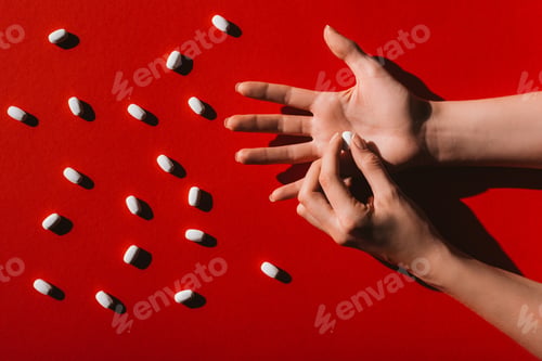 Preview: top view of human hands and white pills on red