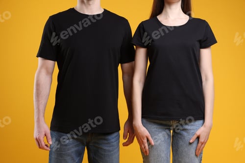 Preview: Woman and man wearing blank black t-shirts on orange background, closeup. Mockup for design
