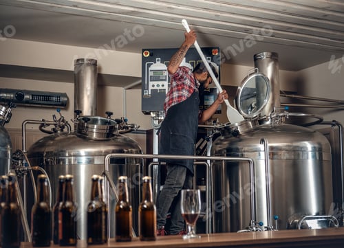 Preview: Indian male manufacturer presenting craft beer in the microbrewery.
