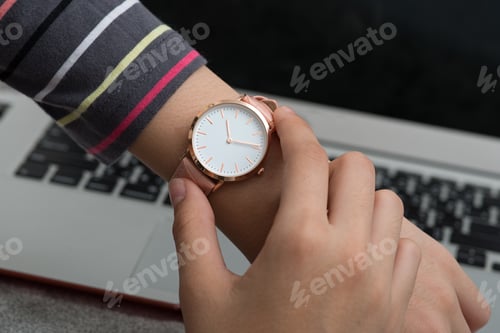 Preview: Girl's hand with wrist watch in front of desk with laptop computer