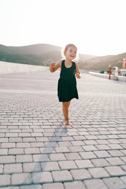 Preview: Little laughing girl walks barefoot on a tiled road, dancing and waving her arms