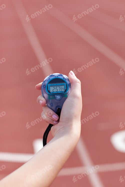 Preview: Translucent blue digital stopwatch with black lanyard ticking in hand above red running track lanes