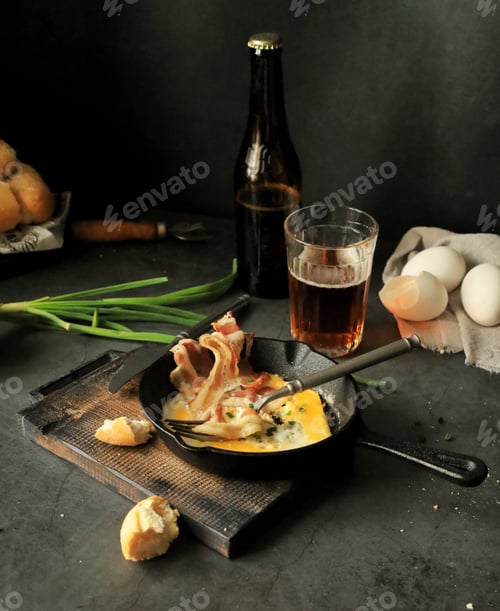 Preview: Fried eggs with bacon in a frying pan on the table, beer and other food products for lunch