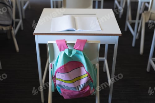 Preview: Backpack hanging on chair at desk with book in classroom