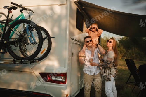 Preview: a young family with glasses is standing next to their mobile home. Dad, mom and daughter together